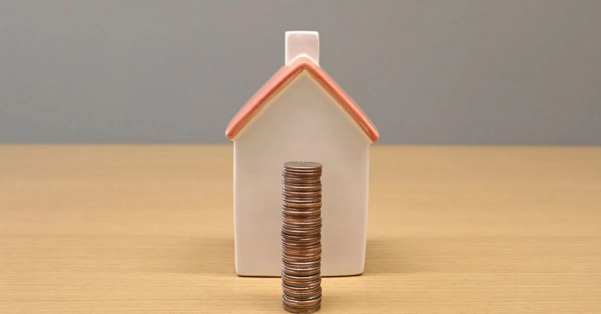 Une image de nature morte conceptuelle de pièces empilées devant une maison en porcelaine, symbolisant l'épargne et l'investissement.