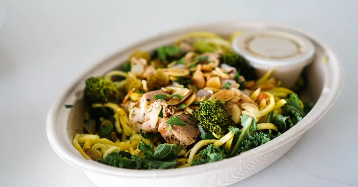 Un délicieux bol de poulet grillé, brocoli et nouilles de courgette garnies d'amandes.