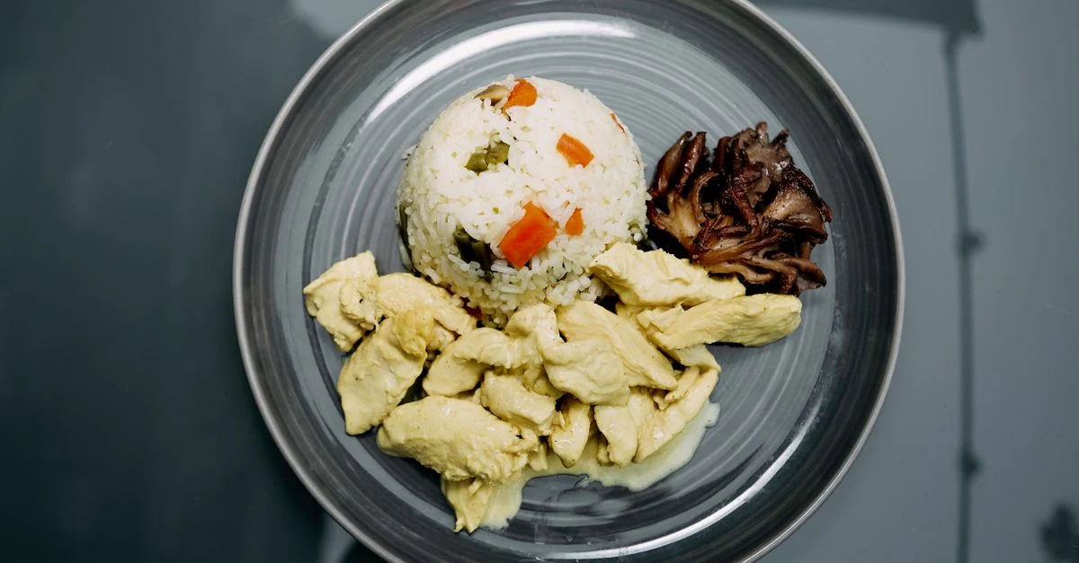 Un repas soigneusement préparé composé de poulet, de riz aux légumes et de champignons sur une assiette en céramique.