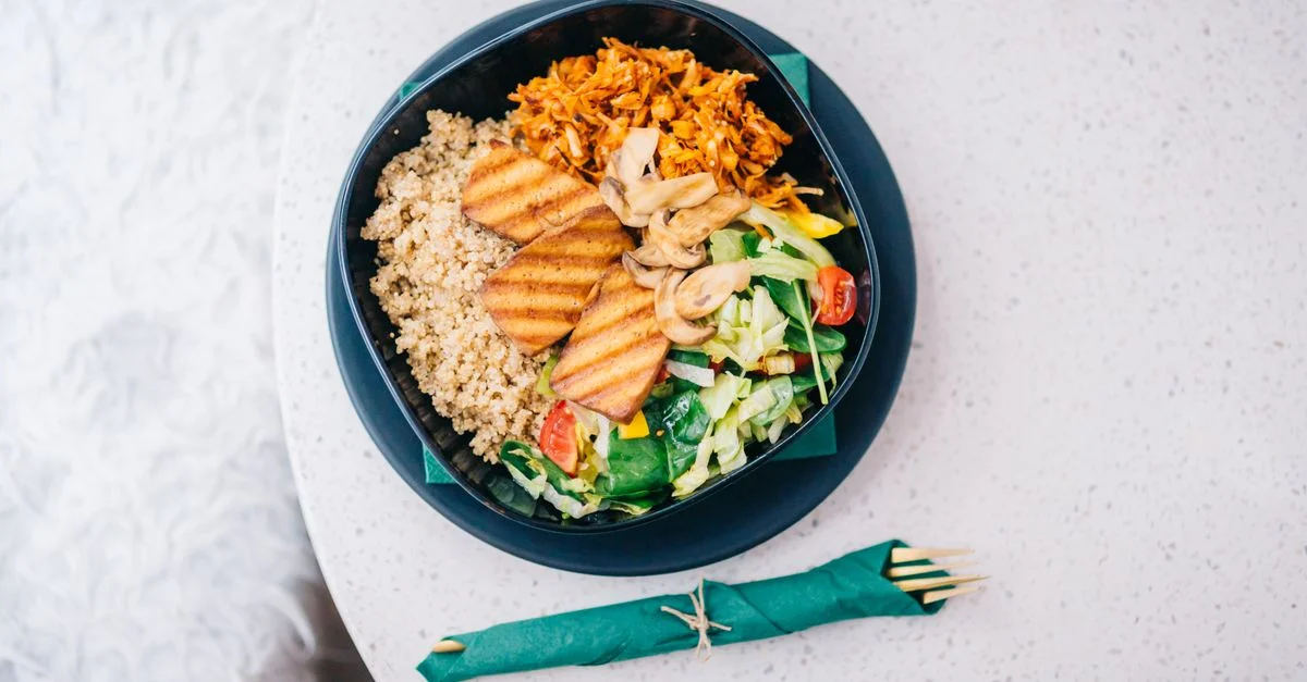 Un bol nutritif avec du tofu grillé, du quinoa, une salade fraîche et des champignons sur un fond clair.