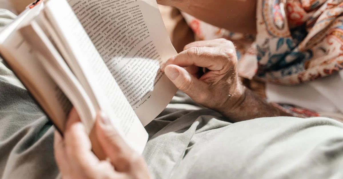 Un gros plan détaillé de mains âgées tenant délicatement et tournant les pages d'un livre ouvert, à l'intérieur.