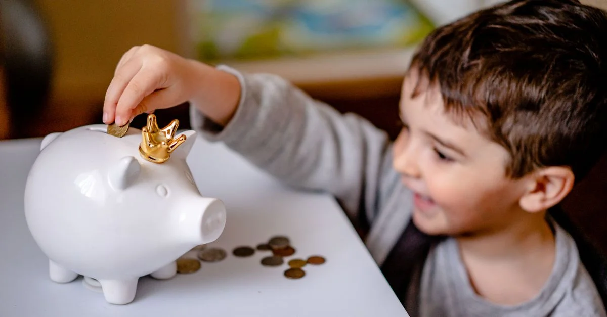 Jeune garçon souriant en train d'épargner de l'argent dans une tirelire couronnée, montrant une responsabilité financière.