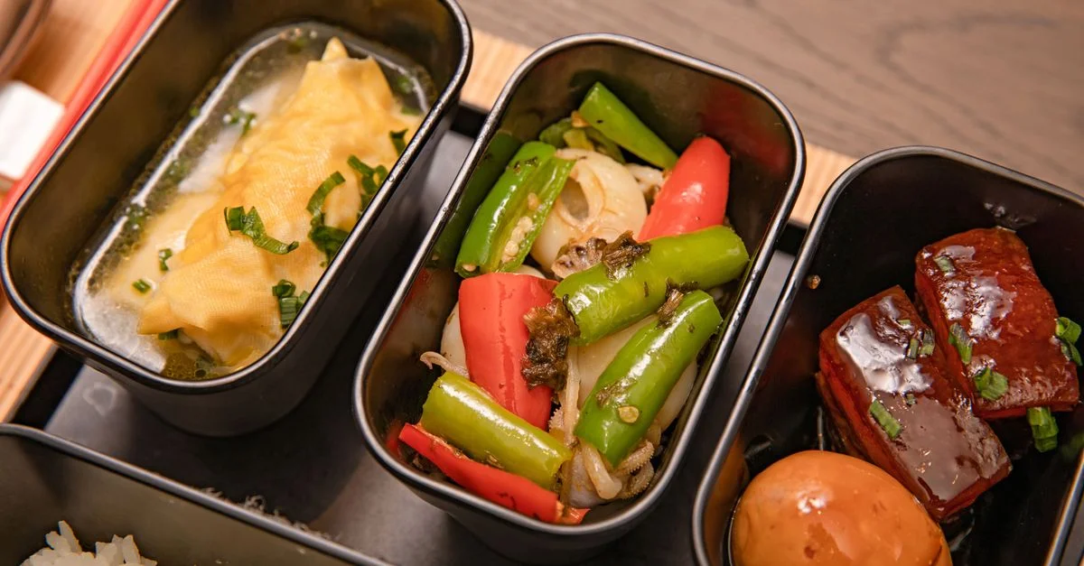Gros plan sur une boîte bento asiatique contenant des raviolis, des légumes et de la poitrine de porc.